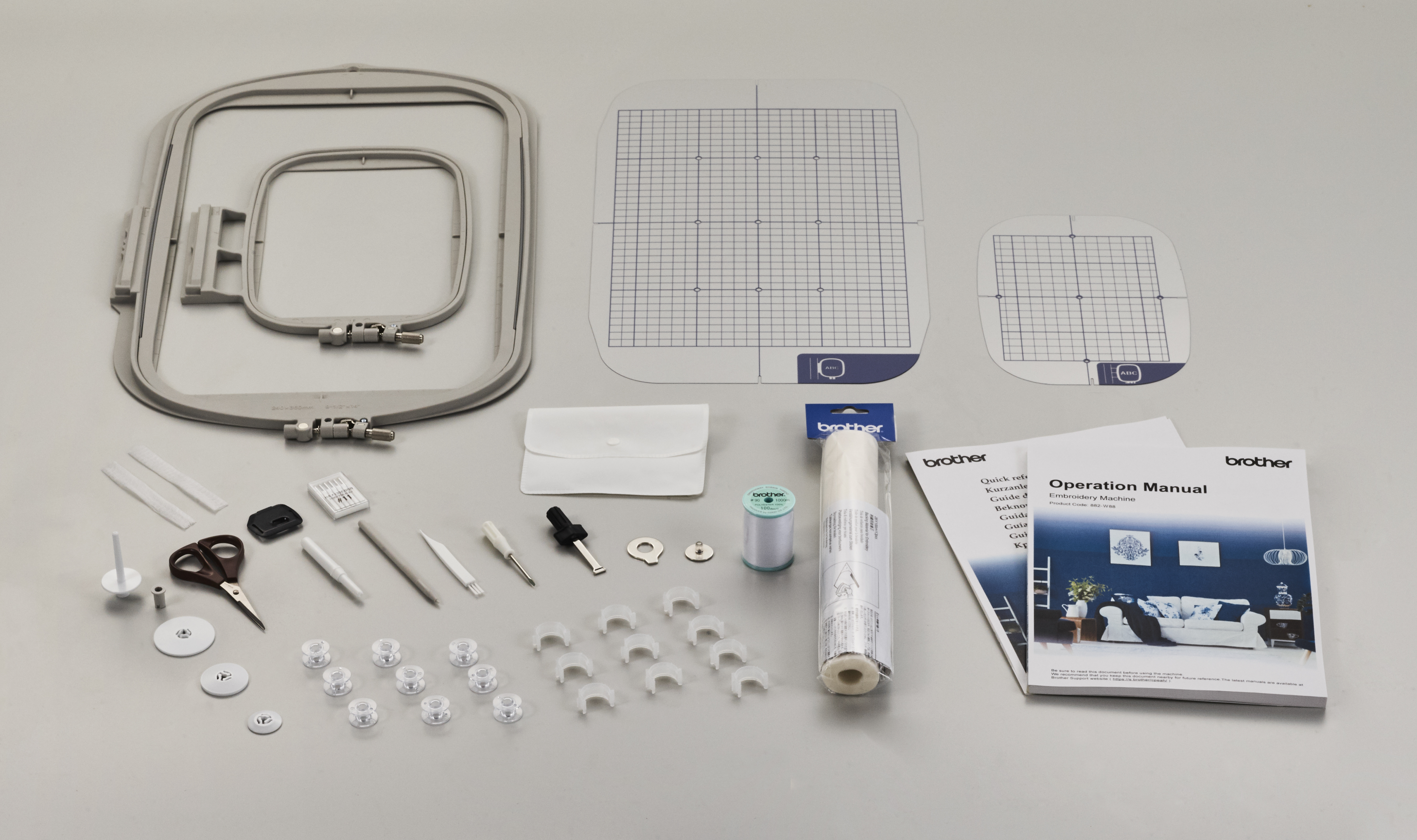 Embroidery machine hoop, needles, thread, and operation manual on a gray background