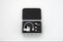 An open gray hard carrying case with black foam insert, containing a small white stitch regulator and several small sewing feet, photographed on a clean white background.