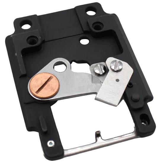 A replacement needle plate, featuring a black plastic housing, silver metal lever arms, and a copper-colored circular component, shown on a plain white background.