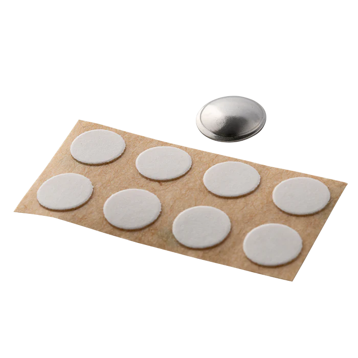 White circular stickers on a brown paper backing with a metal disc above them on a white background
