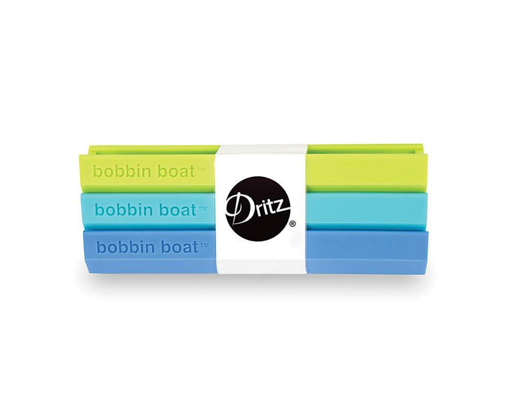 A set of three Dritz Bobbin Boat elastic bands in lime green, light blue, and medium blue, wrapped together with a white paper band featuring the black Dritz logo.