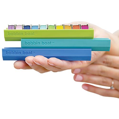 Three colorful bobbin boats held in a hand against a white background