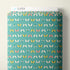 A roll of fabric with a repeating pattern of butterflies and dragonflies on a teal background, with a white header card labeled CLOUD9 at the top, photographed against a plain light wall.