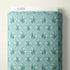 A roll of Cloud9 fabric with a repeating snowdrop pattern on a light teal background, shown against a neutral off-white wall.