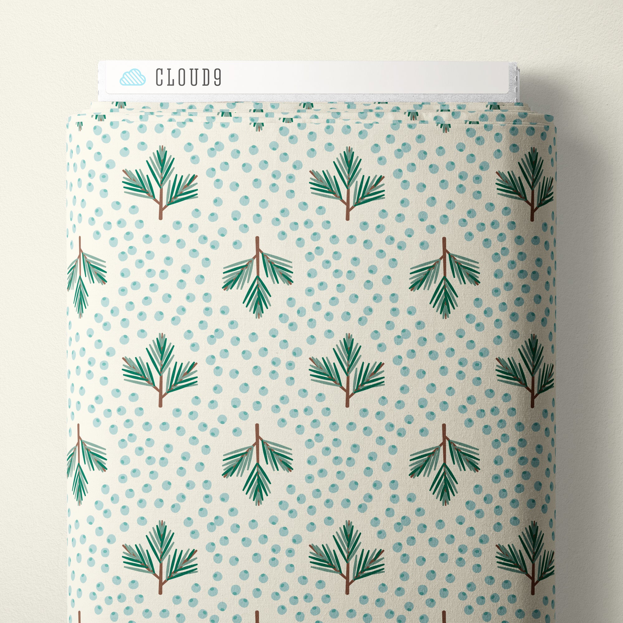 A roll of patterned fabric with a white background, light blue polka dots, and green pine branch motifs, shown with a white Cloud9 paperboard label at the top.
