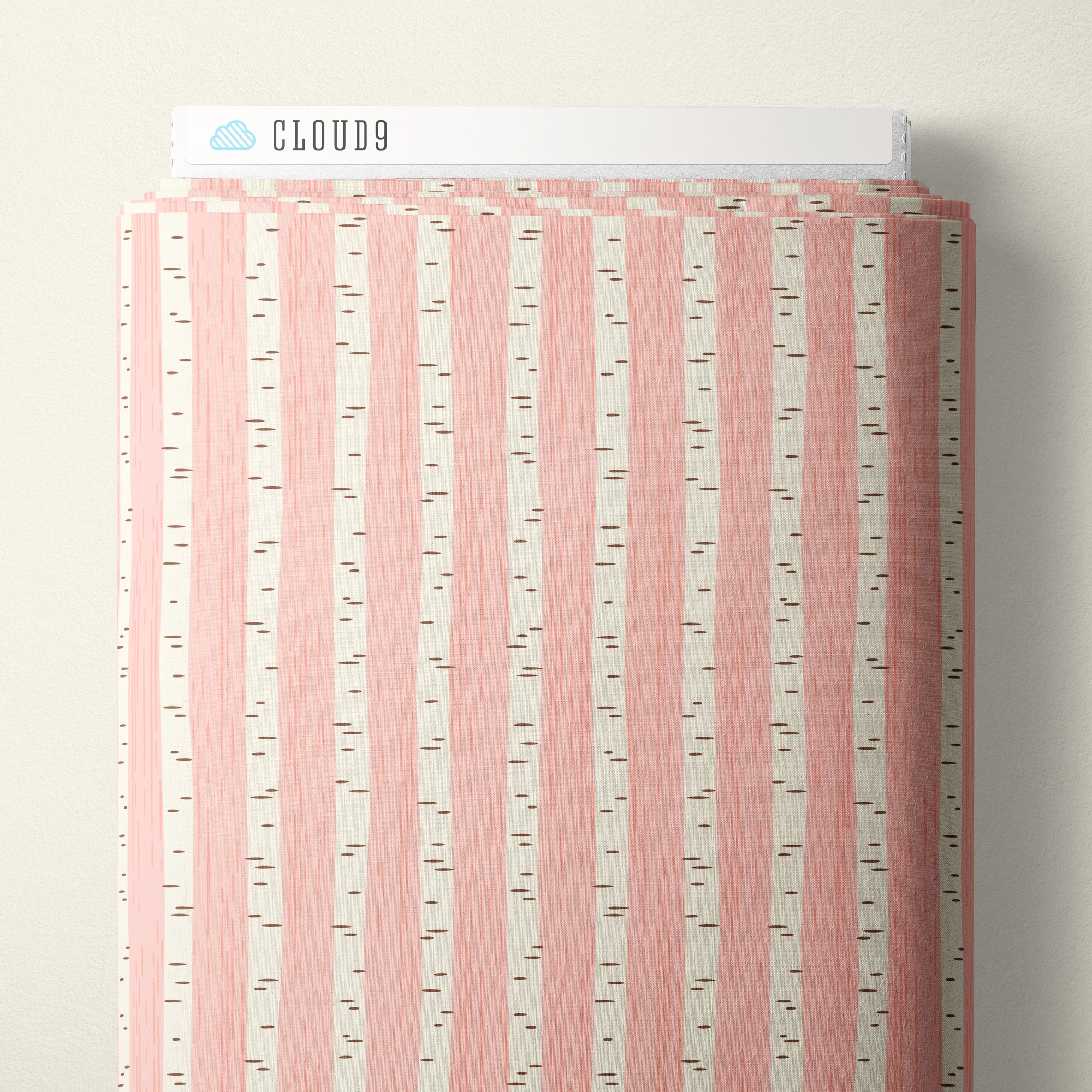 Cloud9 branded fabric bolt with a vertical birch tree pattern in pink and off-white, photographed against a neutral light beige wall.
