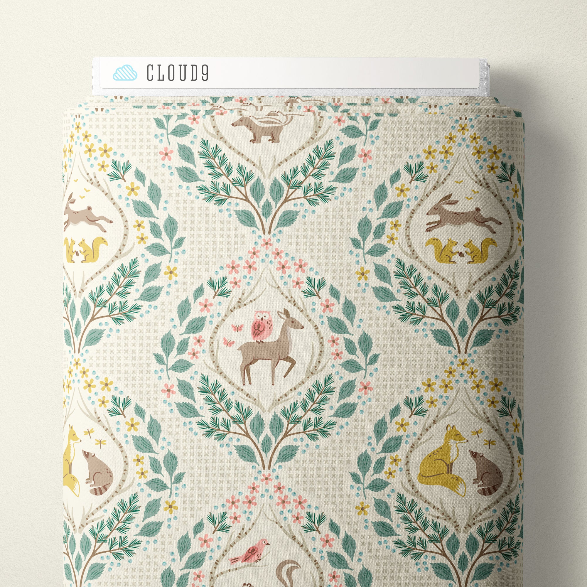 A roll of Cloud9 fabric with a whimsical woodland damask pattern, featuring deer, squirrels, birds, and leaves in muted teal, yellow, pink, and brown on a cream background.
