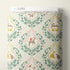 A roll of Cloud9 fabric with a whimsical woodland damask pattern, featuring deer, squirrels, birds, and leaves in muted teal, yellow, pink, and brown on a cream background.