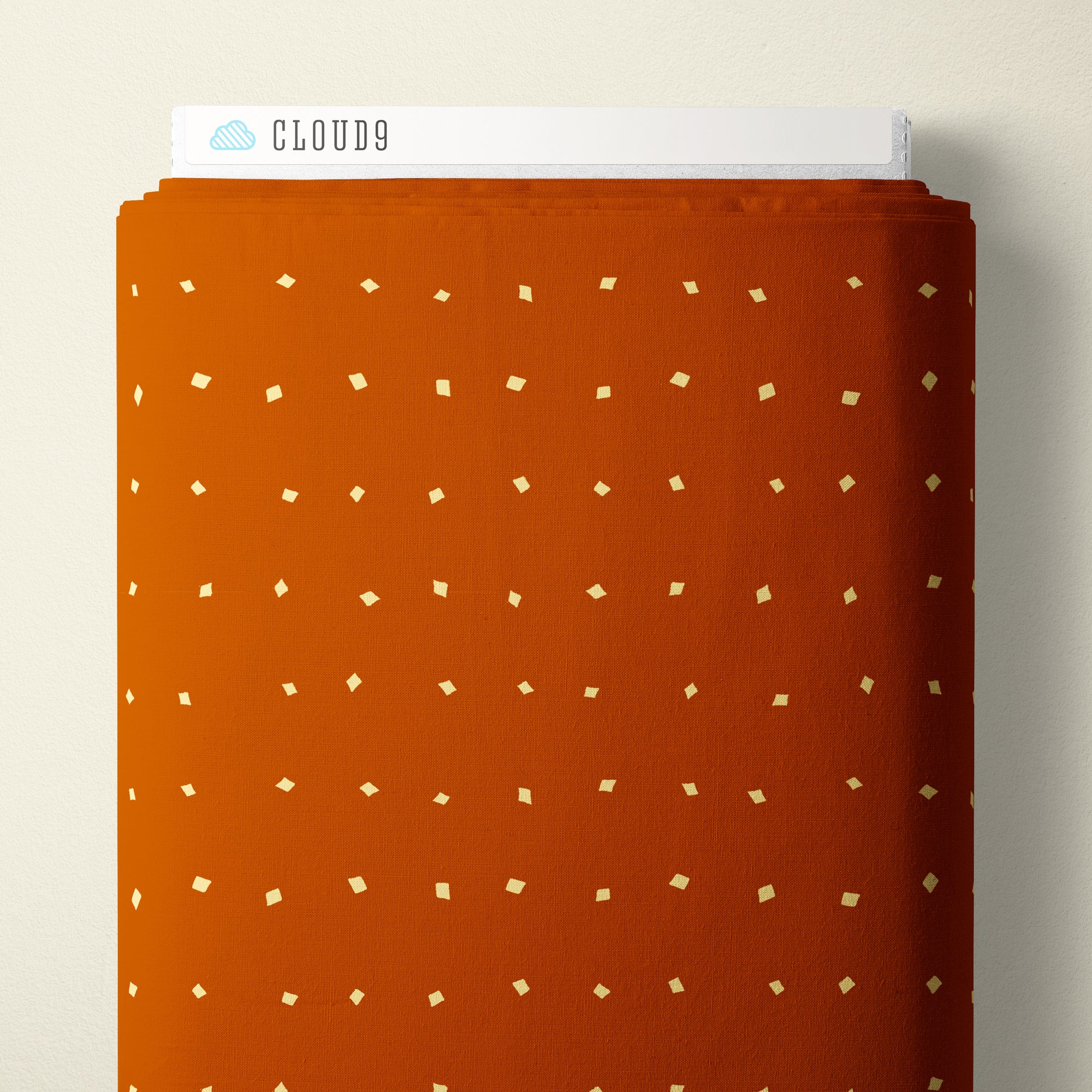 An orange fabric sample with a small white geometric pattern, folded to show its texture and a white header card labeled CLOUD9.