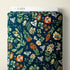 A roll of fabric with a dark teal blue background and a detailed botanical pattern featuring green leaves, orange and cream flowers, and white butterflies. A white cardboard header at the top reads CLOUD9.