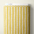 A roll of Cloud9 brand fabric featuring a vertical birch tree pattern in mustard yellow and white, with thin brown branch details, shown against a neutral off-white background.