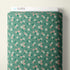 A roll of fabric with a sage green background and a repeating pattern of small white, pink, and green flowers, shown with a white label at the top that reads CLOUD9.