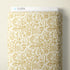 A roll of fabric with a repeating champagne-themed pattern in gold on a warm cream background, shown against a light beige wall. A white header strip at the top reads CLOUD9.