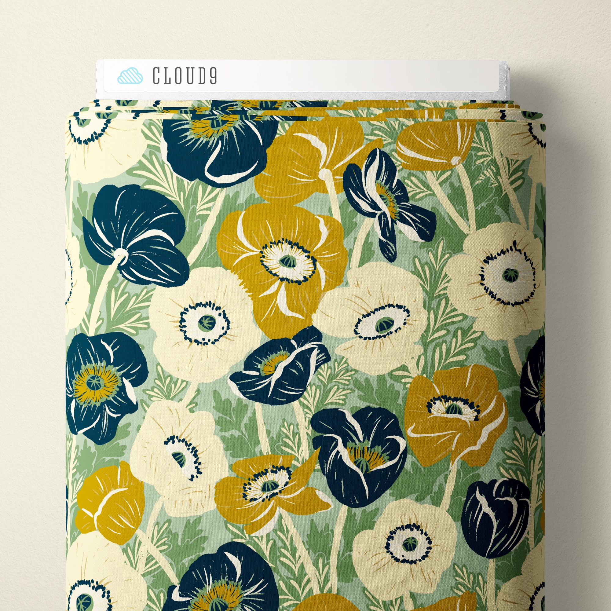 A close-up of a fabric or wallpaper sample with a floral pattern in navy blue, mustard yellow, and cream on a muted sage green background. A white label at the top reads CLOUD9.