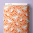 A roll of Cloud9 fabric with a repeating pattern of white flying owls, orange leaves, and small red dots on a peach background, displayed against a light purple wall.