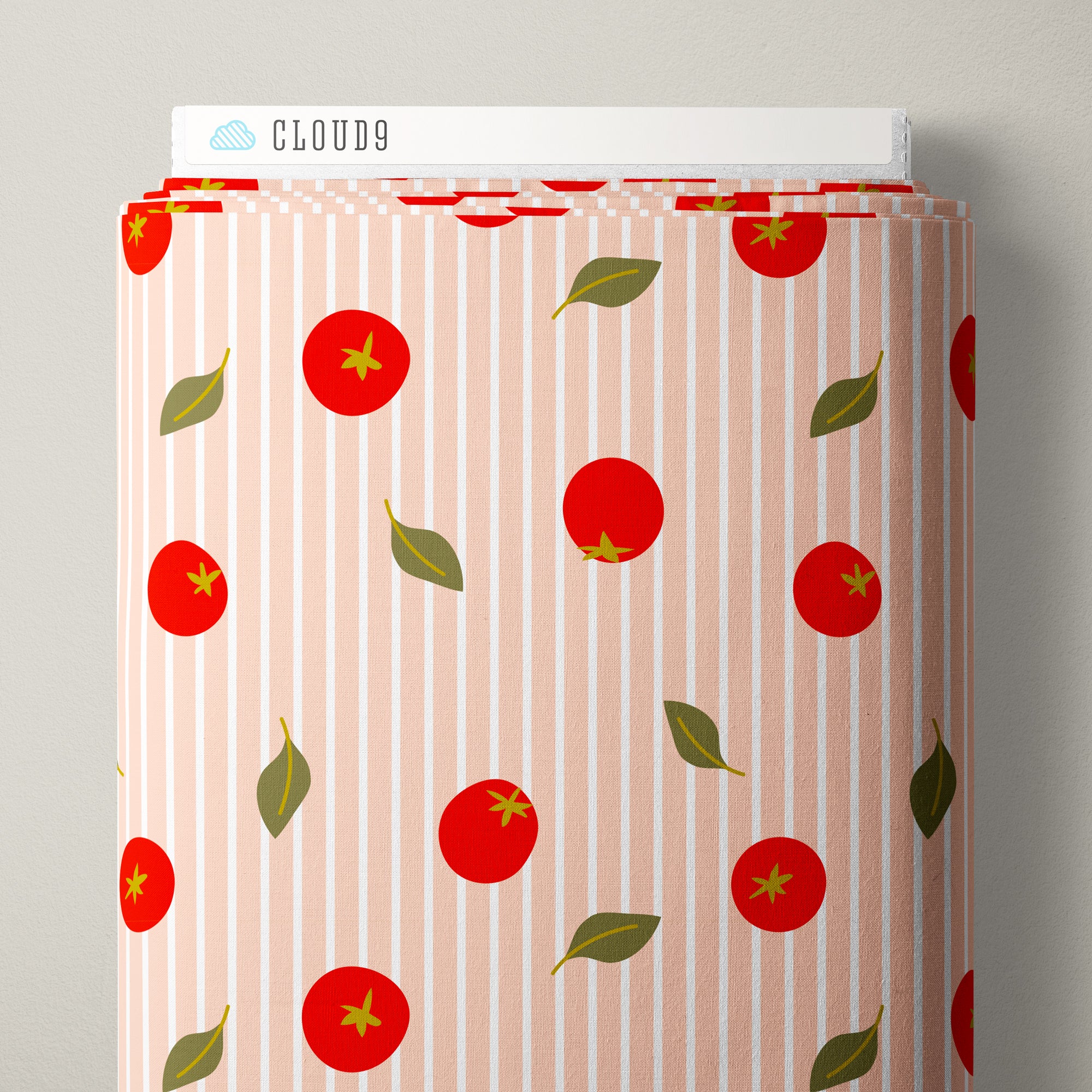 A roll of fabric with a pattern of red tomatoes and green leaves on a light pink and white vertical stripe background, displayed on a neutral gray surface.