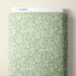 A roll of wrapping paper or fabric with a repeating white line-art pattern of bottles, glasses, and food icons on a pale mint green background, shown against a light neutral wall. A white header card at the top reads CLOUD9.