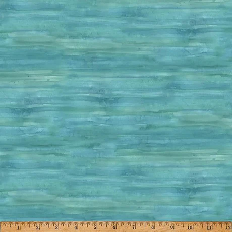 A close-up of a fabric with a watercolor-like textured design in shades of teal, blue, and green, with a wooden ruler along the bottom edge showing measurements.