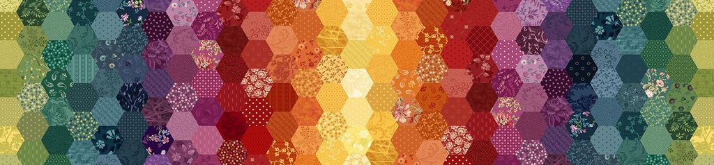A close-up of a quilted fabric pattern featuring hexagonal patches arranged in a rainbow gradient of green, blue, purple, red, orange, and yellow, with various floral and geometric patchwork designs.