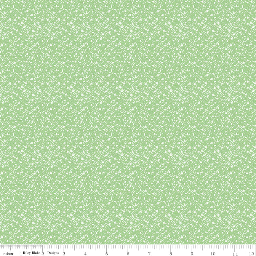 A close-up fabric pattern swatch showing a light sage green background with a repeating small white floral or ditsy dot motif. A ruler along the bottom edge shows measurements in inches and includes the text 'Riley Blake Boutique', indicating the brand.