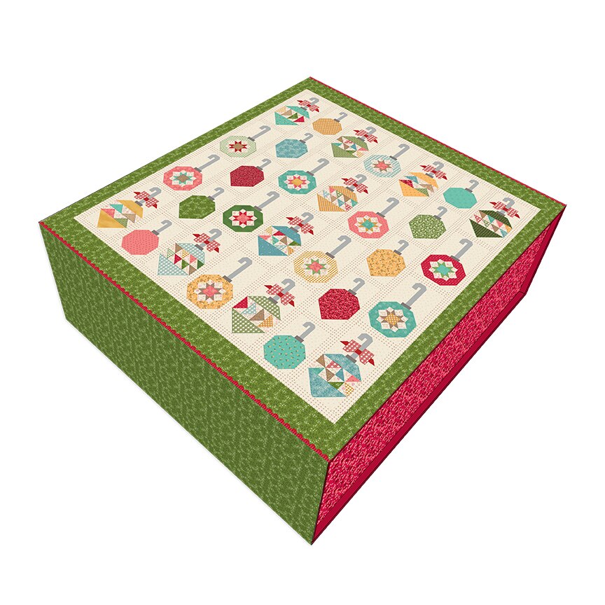 A square quilted fabric box with a colorful patchwork design featuring quilted umbrella motifs on a cream background, bordered by a green patterned top and a red patterned side, shown on a plain white background.