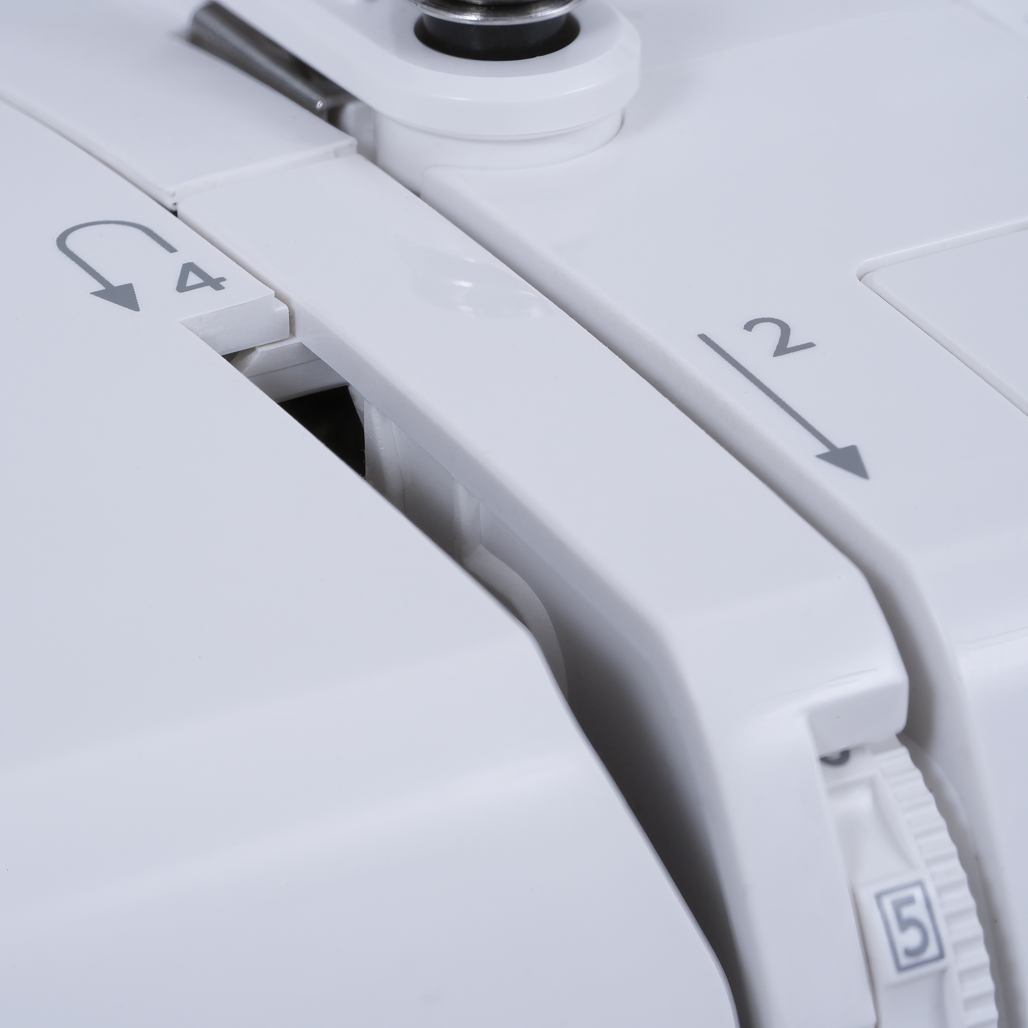 Close-up of a white sewing machine showing control dials and numbered settings including 2, 4, 5, and 6.