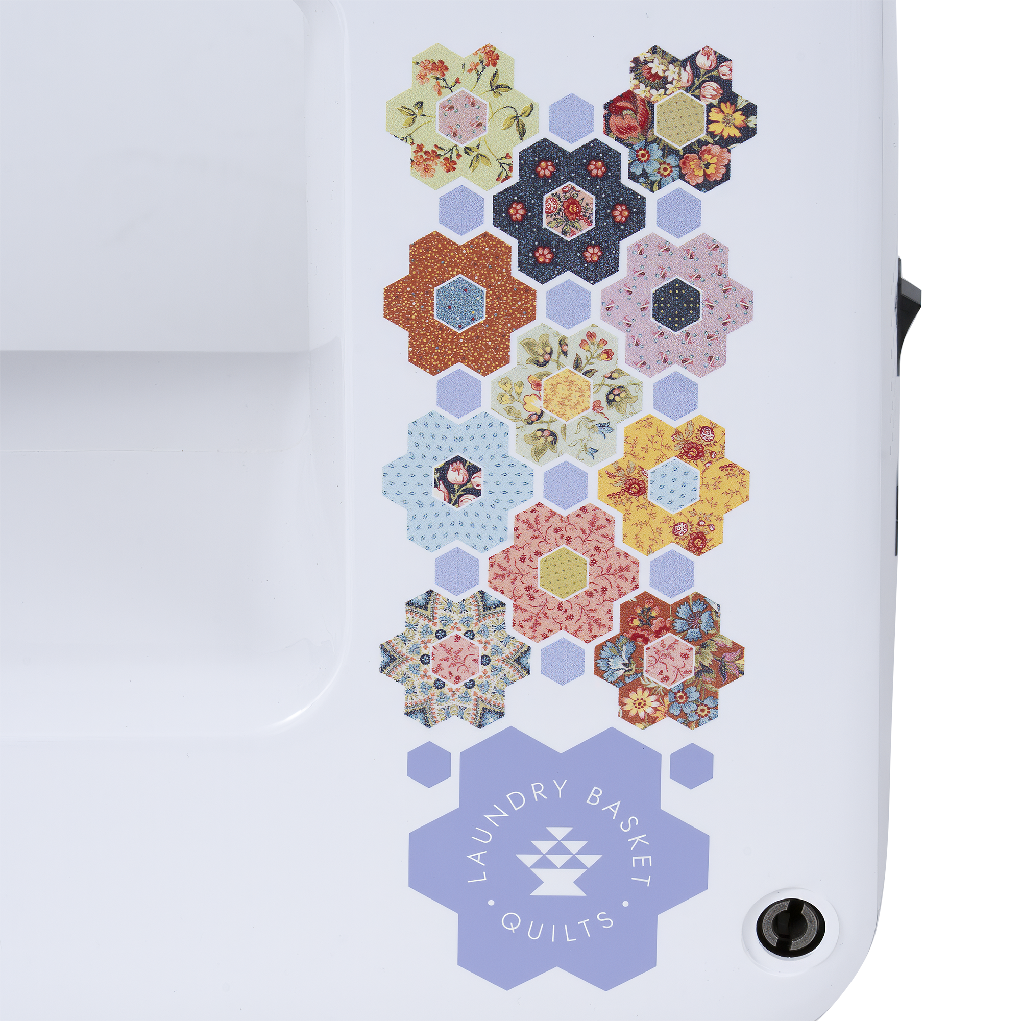 Close-up of a white sewing machine body featuring a vertical decorative pattern of colorful quilted hexagonal motifs and a lavender hexagonal patch labeled 'Laundry Basket Quilts'.