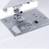 Close-up of a white and silver sewing machine showing the presser foot, needle area, and a transparent fabric measurement guide with size markings.