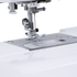 Close-up of a sewing machine needle area with a metallic presser foot, needle, and fabric guide plate on a white sewing machine bed.