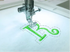 Embroidery machine stitching a green letter 'R' on fabric