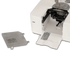 A close-up of a white sewing machine with its front cover open, showing internal components, alongside a detached gray metal plate on a clean white background.