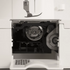 Close-up of a white sewing machine showing the open front cover, internal mechanism, and a metal press foot above the needle area.