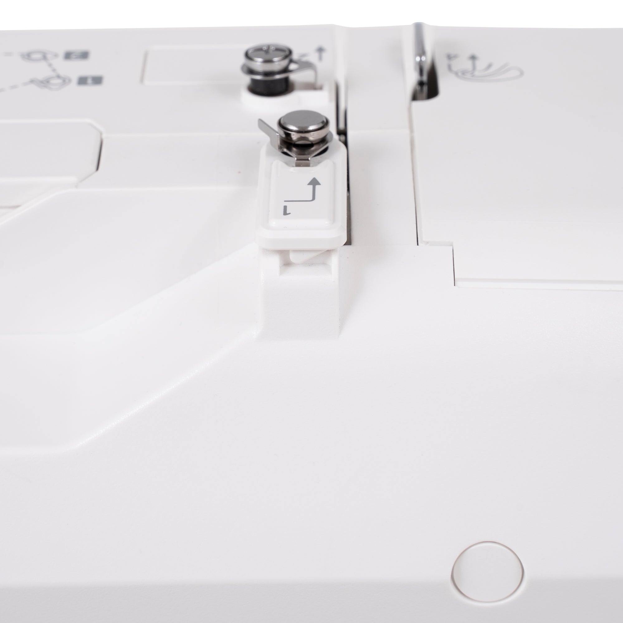 Close-up of a white sewing machine showing the needle area with silver metal tension adjusters and a white plastic guide block with a small printed arrow.