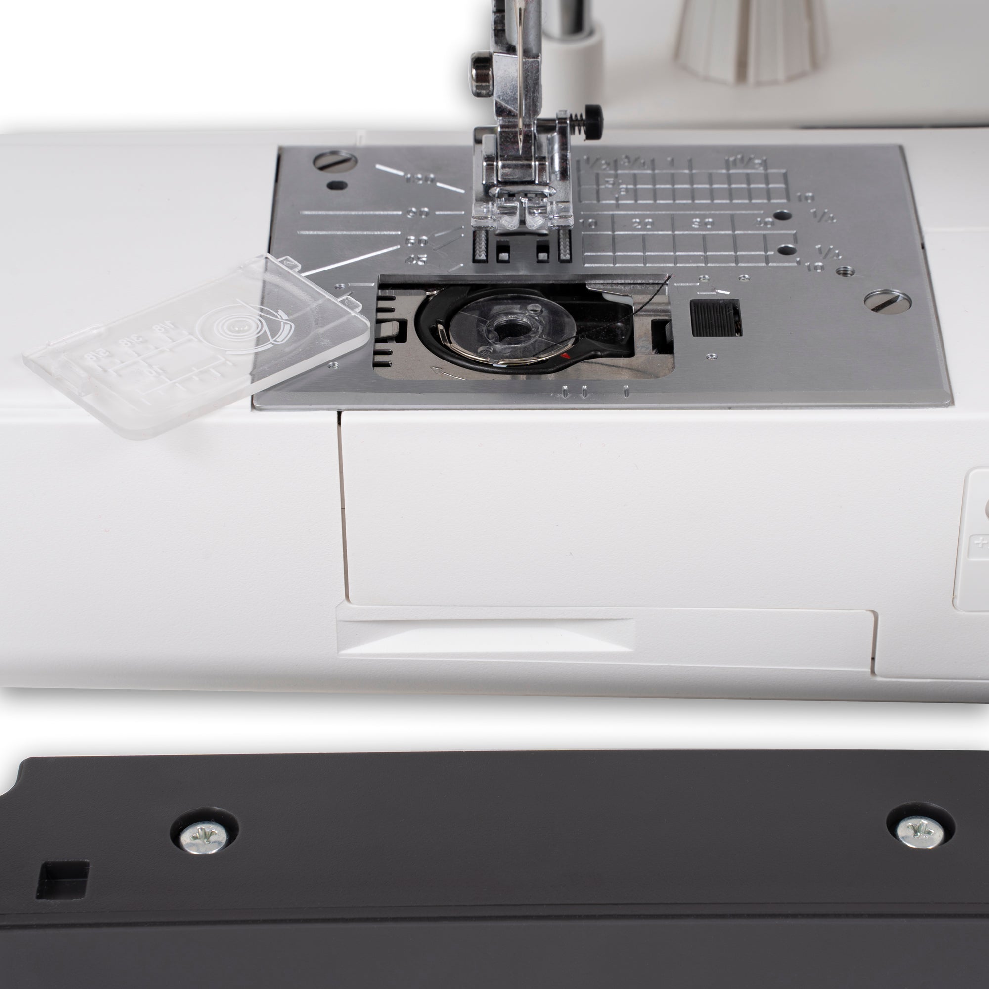 Close-up of a white sewing machine bed with a metal needleplate, presser foot, and a clear plastic cover placed on the left. A black panel with two visible silver screws is shown in the foreground.