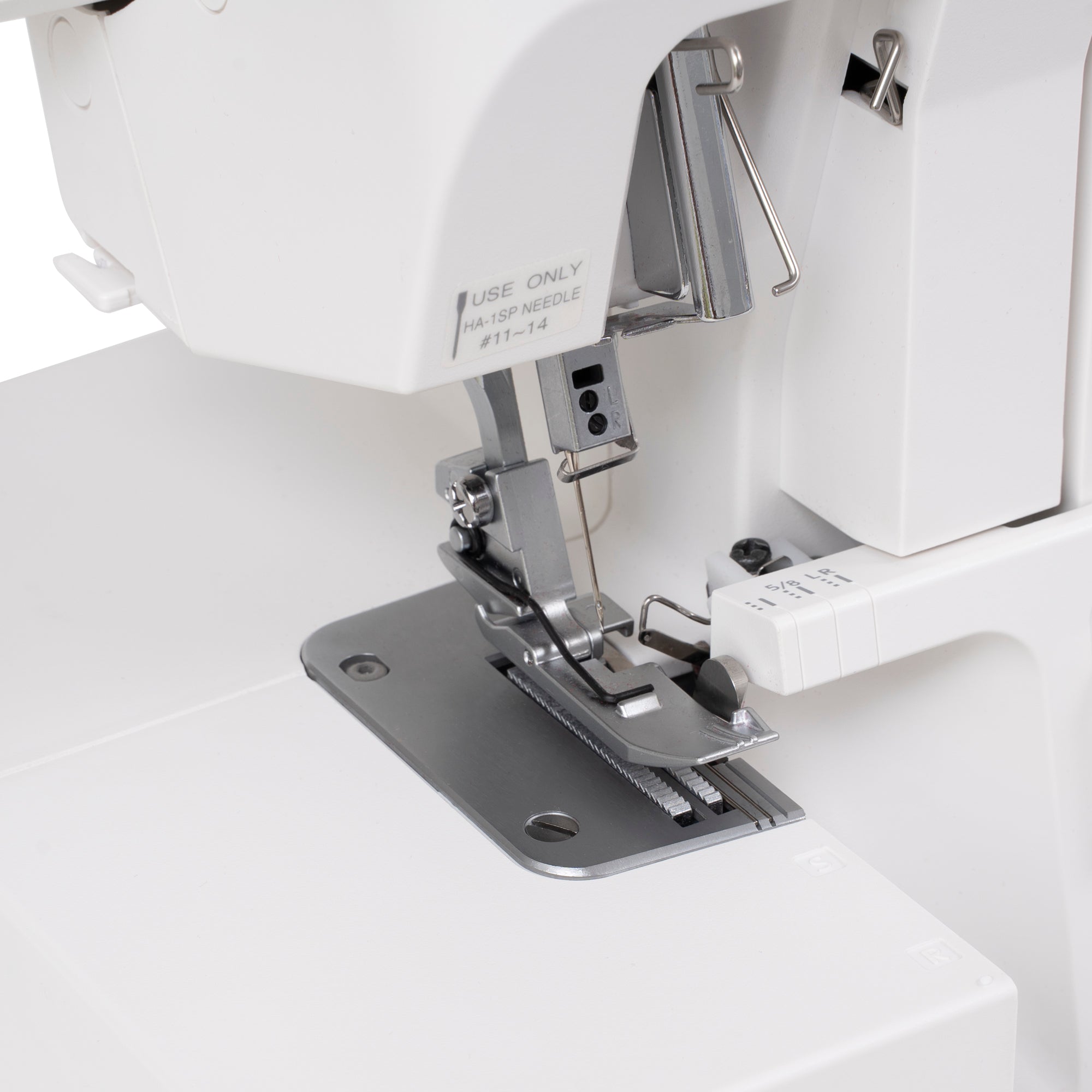 Close-up of a white sewing machine with a metallic presser foot and silver metal plate, showing part of the machine body and a white surface.