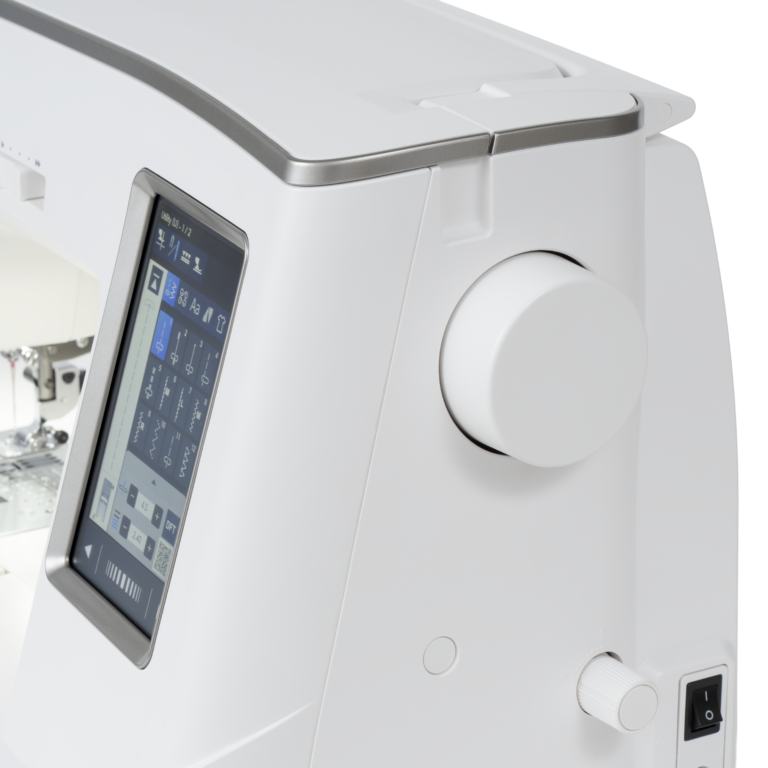 Close-up of a white modern sewing machine showing the top lid, a large white control dial, a touch screen display, and a power switch on a clean white background.