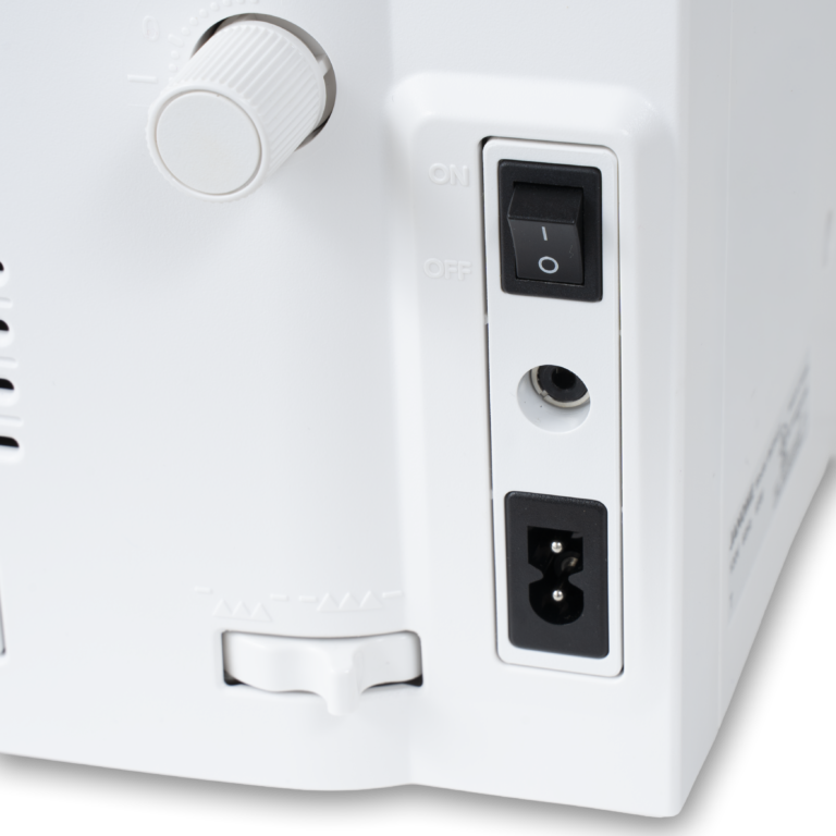 Close-up of the rear control panel of a white sewing machine, showing a white rotary knob, a black power switch, a grounding hole, a power outlet, and a white slide switch.