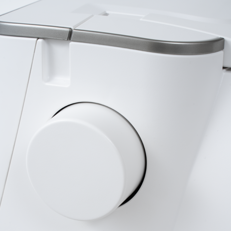 Close-up of a white sewing machine with a circular control dial and a metallic silver trim along the top edge.