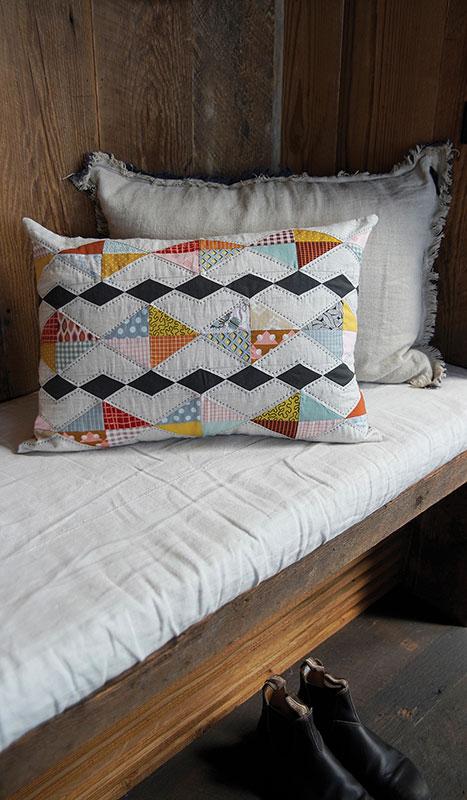 Decorative pillow with geometric pattern on a wooden bench against a wooden wall.