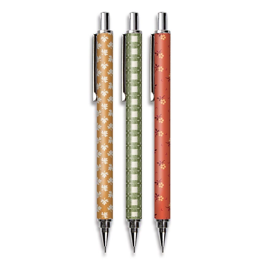 Three retractable mechanical pencils with decorative patterned barrels, shown vertically on a plain white background. The left pen has a warm orange-brown background with white floral motifs; the middle pen has an olive green and white checkered pattern; the right pen has a coral-red background with small pink floral motifs.