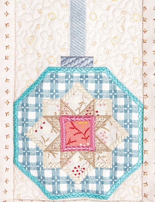 A close-up of a quilted fabric ornament patch with a geometric star design in light blue, teal, pink, and cream, attached to a matching quilted textile background.
