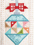 A close-up of a quilted fabric ornament design with a red bow at the top, a light blue diamond-shaped body, and multicolored triangular patchwork sections including pink, green, orange, beige, and brown.