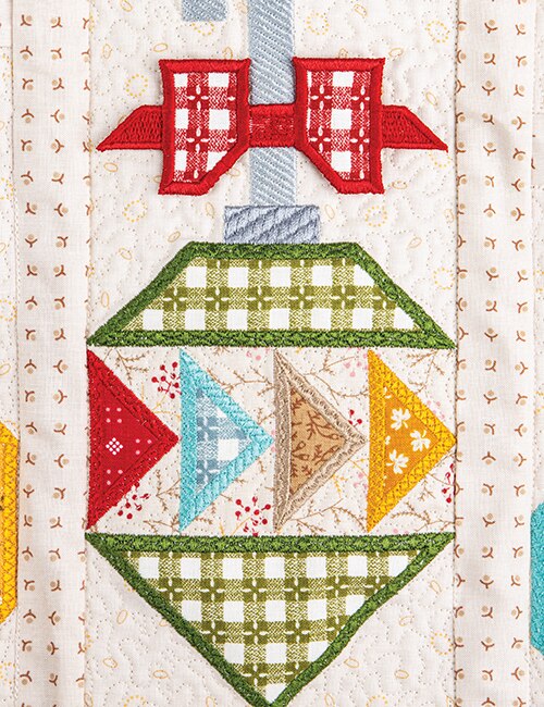 A close-up of a quilted textile featuring a stylized Christmas ornament design with red bows, green plaid sections, blue and yellow triangles, and an off-white quilted background.