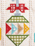A close-up of a quilted textile featuring a stylized Christmas ornament design with red bows, green plaid sections, blue and yellow triangles, and an off-white quilted background.