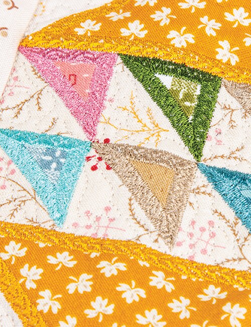 Close-up of a colorful embroidered patchwork quilt with triangular fabric sections in pink, green, blue, beige, and yellow floral patterns.