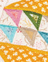 Close-up of a colorful embroidered patchwork quilt with triangular fabric sections in pink, green, blue, beige, and yellow floral patterns.