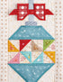 A close-up of a quilted ornament design featuring a red bow at the top, a light blue upper section, and a multicolored geometric patterned lower section on a cream quilted background.