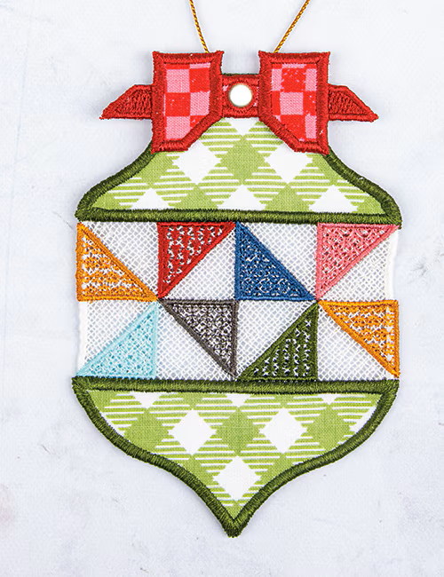 A decorative embroidered ornament shaped like a Christmas tree, featuring a red checkered bow at the top, green and white diamond patterns on the upper and lower sections, and multicolored geometric triangles in the center including red, blue, pink, orange, light blue, gray, and olive green.