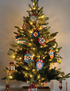 A decorated Christmas tree with warm white string lights and colorful quilt-patterned ornaments hanging from the branches against a plain indoor wall.