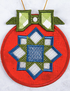 A circular embroidered ornament with a red base, a blue and green geometric star design, and a green bow at the top, shown against a light textured background.
